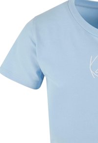 Lyseblå bomull t-skjorte med rund hals og korte ermer. Har et hvitt brodert logo på forsiden. Glatt tekstur.