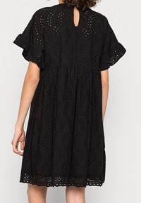 Vestido de algodón negro con mangas cortas con volantes y un escote en forma de ojo de cerradura. Presenta bordado de ojales y un dobladillo decorativo. Diseño acampanado en línea A.