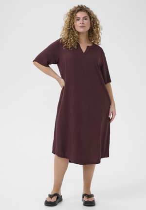 Burgundy dress with short sleeves and a V-neckline. Made of soft fabric, it features a loose fit and side pockets. Black slide sandals.
