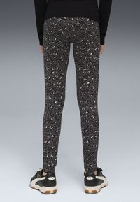 Leggings neri con una fantasia a macchie di leopardo grigia, vestibilità slim e tessuto morbido. Abbinati a scarpe da ginnastica in bianco e nero.