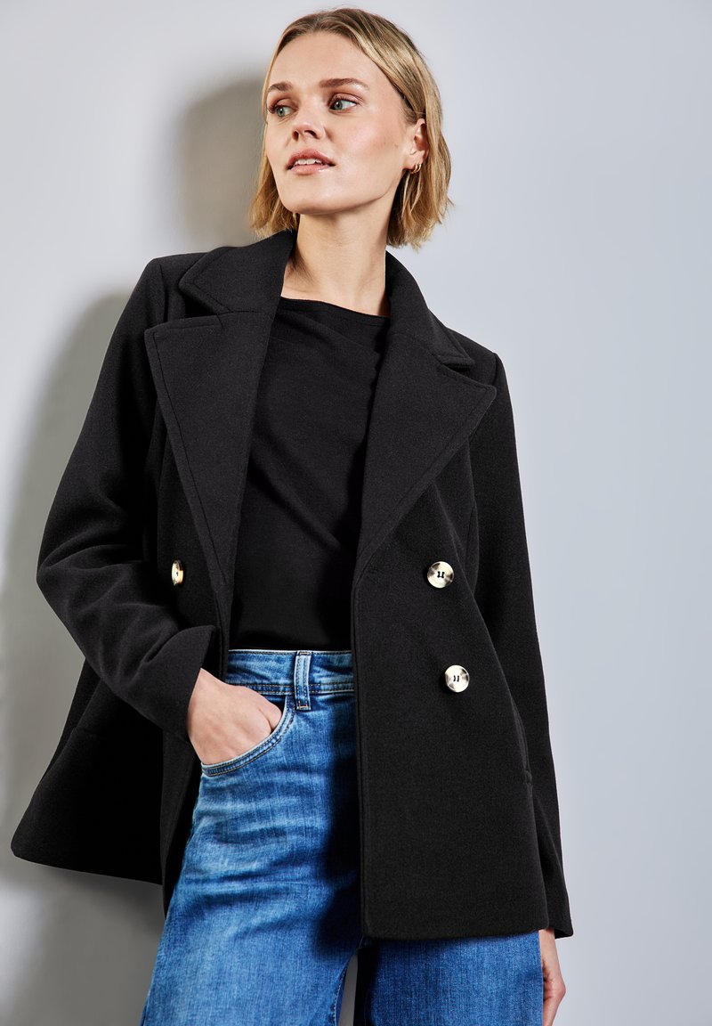 Abrigo peacoat de mezcla de lana negra con frente de doble botonadura, grandes botones dorados, cuello con muesca y corte relajado. Combinado con jeans azules.