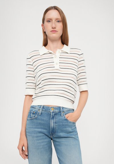 Witte gebreide polo met horizontale strepen in zwart en rood, voorzien van een kraag, drie knopen en korte mouwen. Gecombineerd met lichtblauwe jeans.