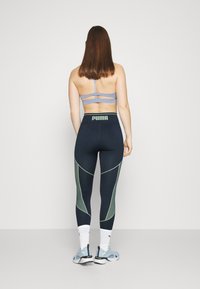Reggiseno sportivo blu con spalline incrociate, abbinato a leggins blu navy con accenti verdi e una vita alta con un logo. Footwear leggero.