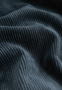 Tissu en velours côtelé bleu foncé avec des côtes verticales douces et surélevées et des plis légers créant une surface texturée et ondulée.