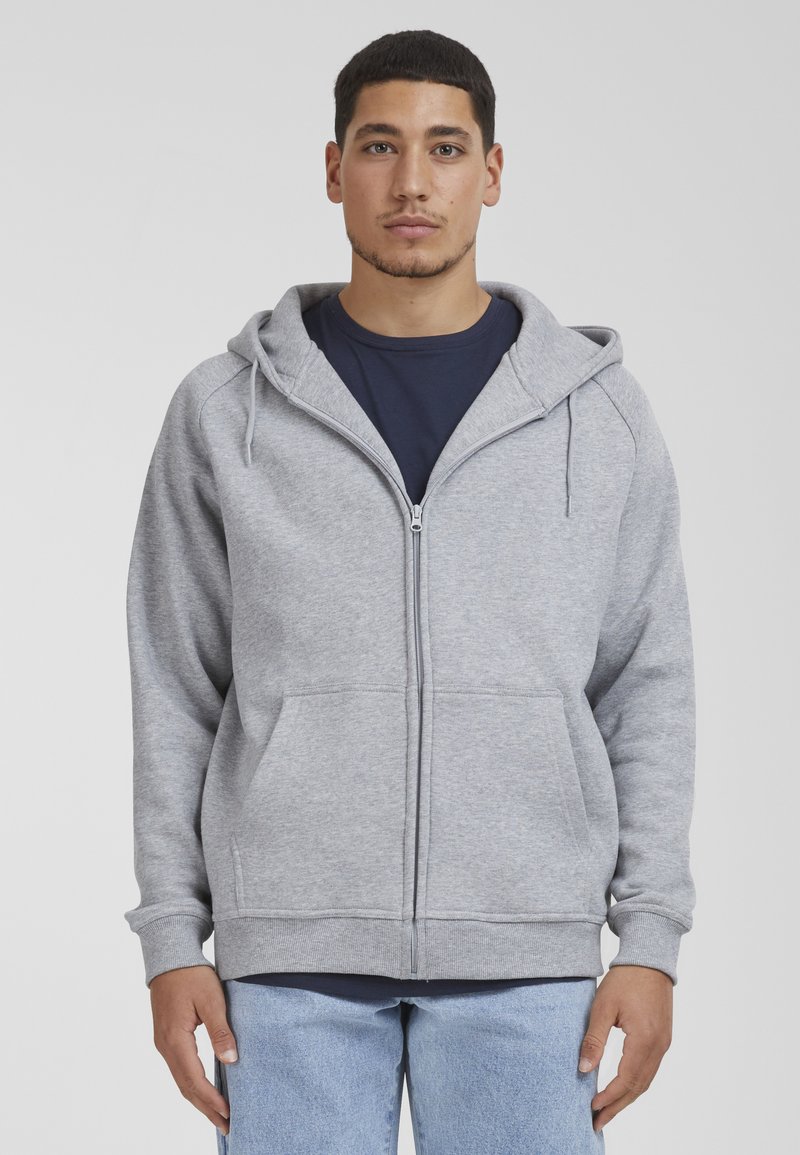 Gray zip-up hoodie with a drawstring hood, front pockets, ribbed cuffs, and a soft texture, worn over a navy shirt and blue jeans.