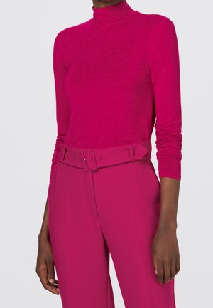 Vrouw draagt een felroze coltrui die is ingestopt in een high-waisted bijpassende broek met een brede riem.