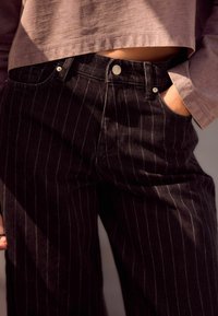 Černé pruhované džíny vyrobené z denimu, s vysokým pasem, předními kapsami a kovovými doplňky. Stylizované s volně padnoucím topem.