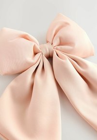 Grand nœud en tissu rose doux avec de larges boucles et de longues queues, posé sur une surface plane claire.