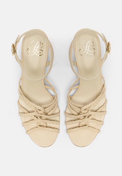 Sandales beige à lanières avec des détails tressés, un design à bout ouvert et une sangle de cheville réglable avec une boucle dorée.