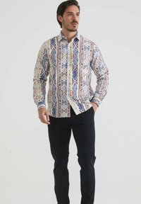 Chemise à manches longues avec boutonnières en blanc ornée de motifs géométriques bleus, rouges et jaunes. Dispose d'un col classique et d'une poche poitrine.