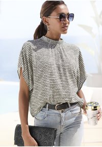 Blusa a maniche corte a fantasia bianca e nera, abbinata a jeans azzurri, una clutch perforata nera e una tazza con motivo marmorizzato.