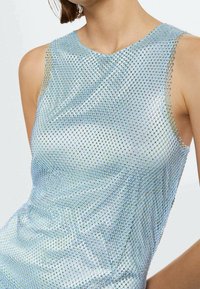 Débardeur irisé bleu sans manches présentant un design en maille avec de petites sequins réfléchissants, une texture douce et un col rond.