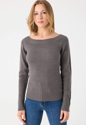 Suéter gris de punto con un escote amplio, puños acanalados y dobladillo inferior. Textura suave con una silueta ajustada. Llevado sobre jeans azules.