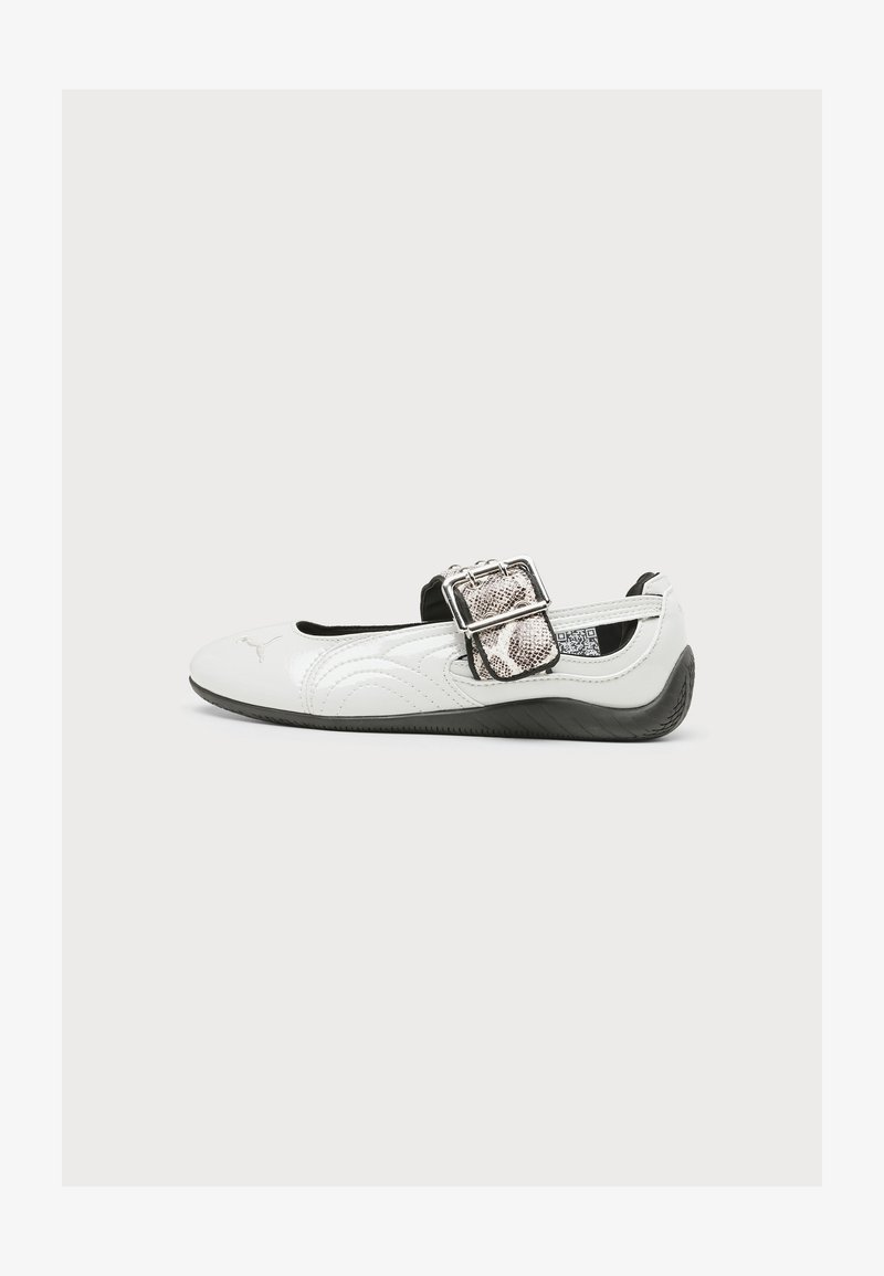 Λευκό επίπεδο παπούτσι με μαύρη σόλα, μεγάλο ασημένιο λουράκι με σχέδιο φίδι και λογότυπο Puma στο μπροστινό μέρος.