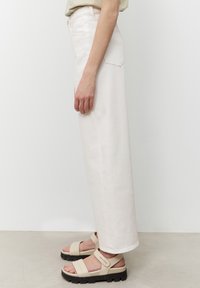 Vita bredbeniga jeans med hög midja, tillverkade av denim. Kombinerat med beige sandaler med kraftiga sulor och justerbara remmar.