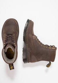 Botas de cuero marrón con acabado texturizado, punta redonda y diseño de cordones. Suela de goma con costuras amarillas y una lengüeta en el talón.