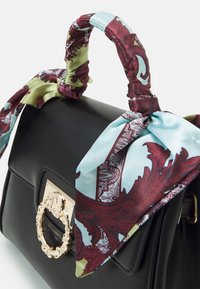 Svart läderhandväska med ett guldaccentlås och en tvåtonad satinhalsduk i blått och vinröd knuten runt handtaget.