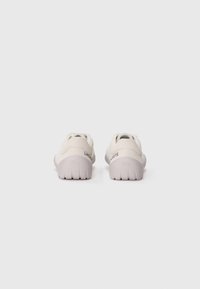 Lacoste sneakers, beige overdel, tekstureret materiale, rund tå, kontrasterende grå sål, branding på hælen, lavprofil design.
