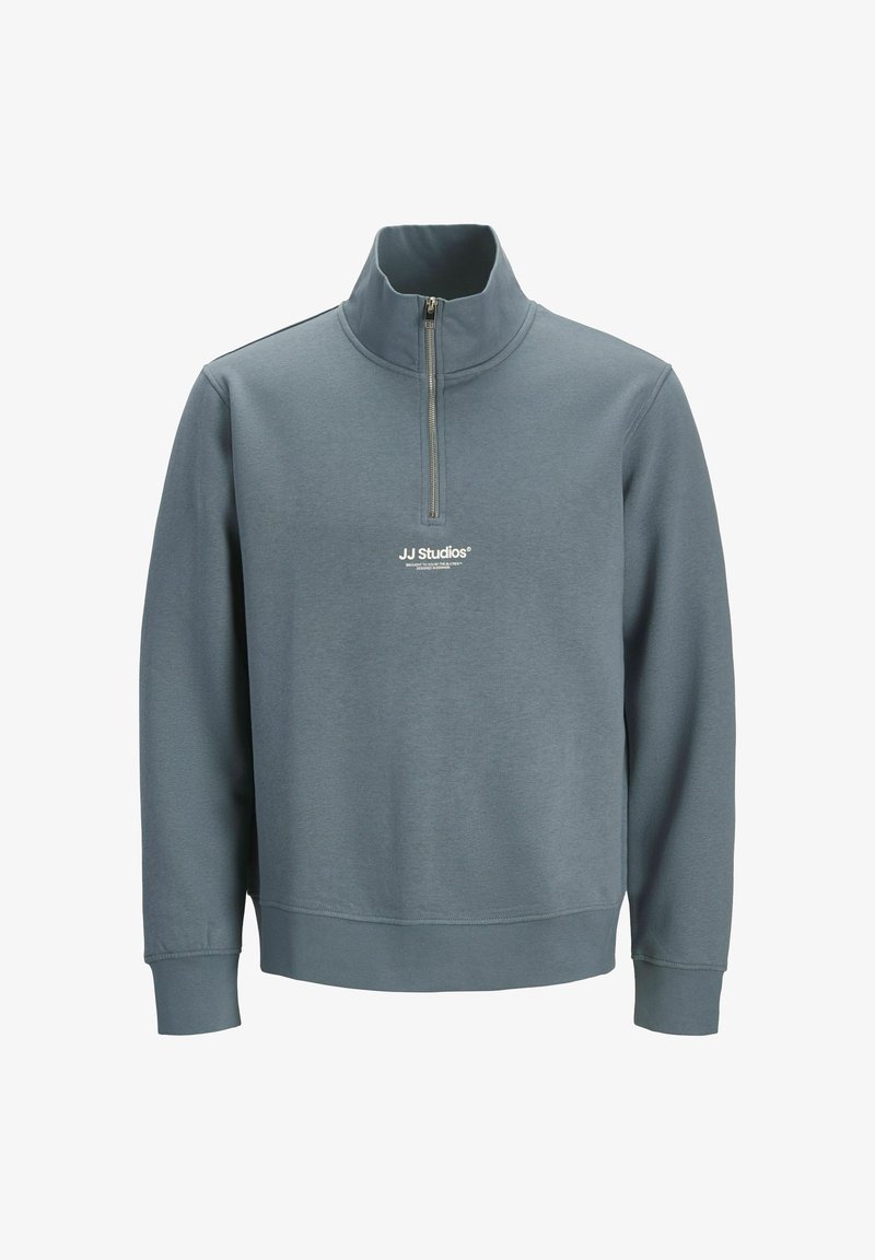 Pilkos spalvos puloveris su pusiau užtrauktuku, pagamintas iš tekstūruotos medžiagos. Siunčiamas su standžio stiliaus apykakle ir baltu logotipu ant krūtinės. Ilgos rankovės su raštuotais manžetais.