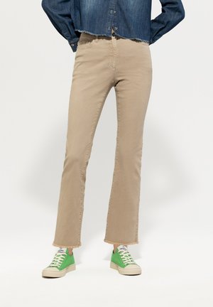Beige flared jeans with a raw hem, paired with green sneakers. The jeans feature a classic five-pocket design and stitched detailing.