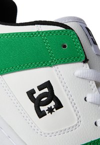White sneaker with green suede accents, black stitching, and a black logo. Features a smooth leather texture and round laces.