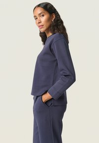 Sudadera azul marino con un ajuste relajado, cuello redondo y mangas largas. Presenta una textura suave y un dobladillo ligeramente curvado.