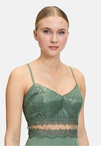 Braletka w szmaragdowym zielonym kolorze z delikatnym koronkowym wykończeniem i cekinami. Posiada regulowane ramiączka oraz kwiatowy wzór koronki w talii.