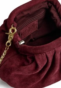 Bordó színű, velúr táska belső rész cipzáras zsebbel és aranyszínű fémes elemekkel, puha tapintású, összegyűrt dizájn részlettel.