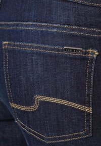 Jeans de mezclilla azul oscuro con un bolsillo trasero con costuras amarillas, una etiqueta característica y una forma de bolsillo clásica.