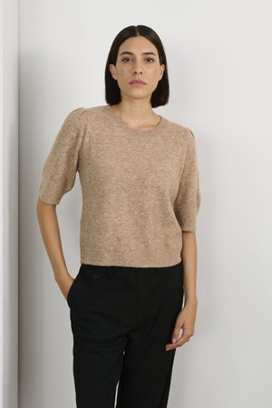 Beige short-sleeve sweater with a round neckline and textured knit. Worn with black trousers featuring side pockets and a button detail.