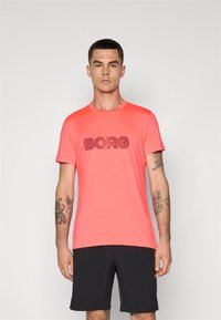 Kortermet korall T-skjorte med "BORG" trykt i en mørkere nyanse, sammen med svarte shorts. Glatt stoff og standard passform.