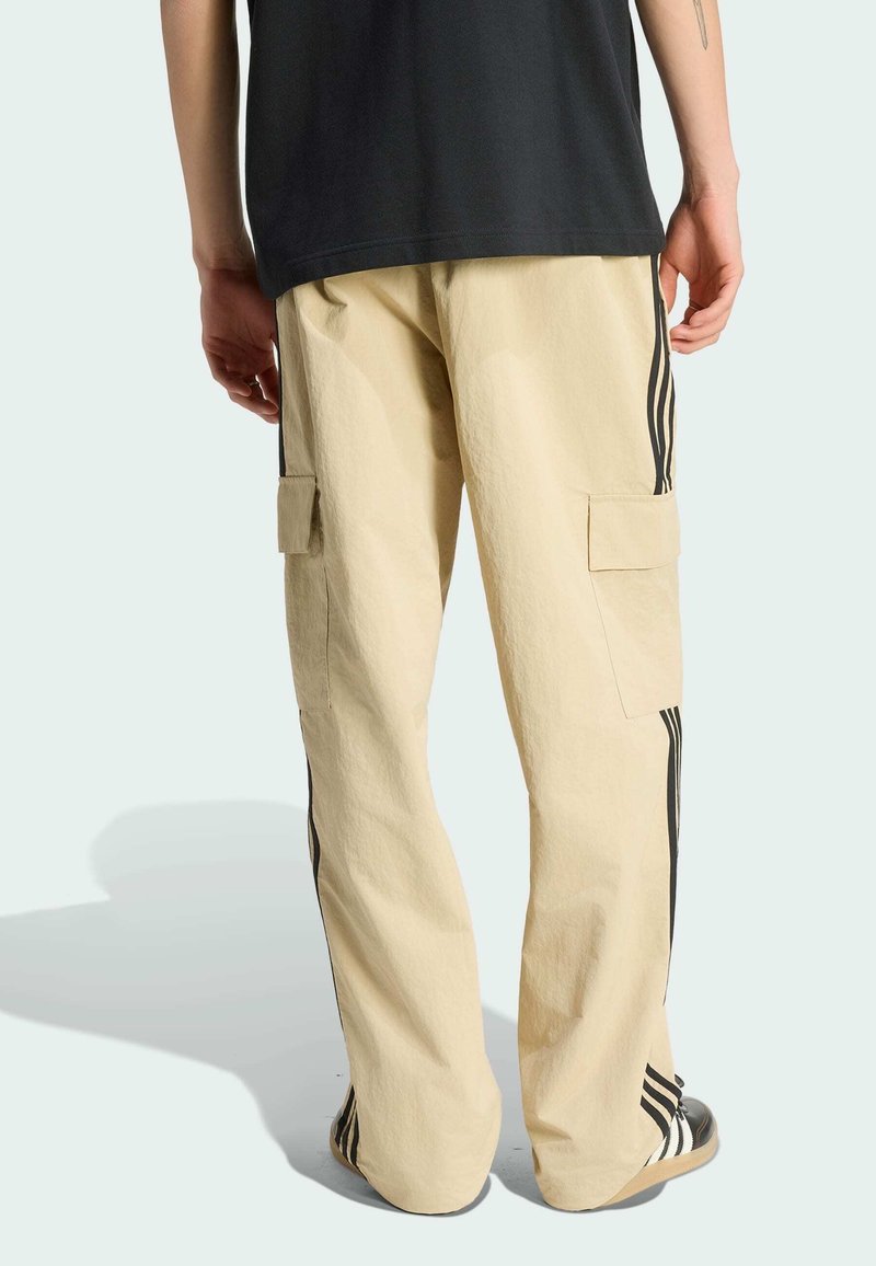 Beige Cargo-Hosen aus leichtem Material, mit schwarzen Seitenstreifen, zwei Seitentaschen und einem lässigen Schnitt.