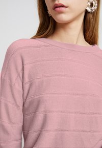 Maglione rosa a maglia con strisce orizzontali, un ampio scollo e dettagli testurizzati sottili. Tessuto morbido con una vestibilità comoda.