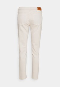 Beige slim-fit jeans met een gladde textuur, voorzien van een bruine leren label op de tailleband en twee achterzakken met een subtiele stikselafwerking.