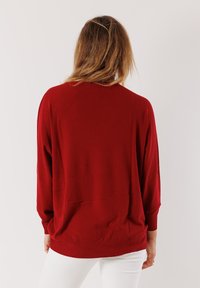 Maglione rosso a maglia con vestibilità morbida, polsini e orlo a coste, spalle scese. Texture liscia, con un design semplice e senza decorazioni.