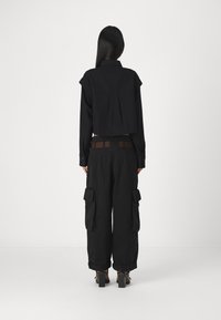 Černá zkrácená košile s drapérií na zádech a dlouhými rukávy, spárovaná s volnými černými cargo kalhotami s bočními kapsami a hnědým páskem.
