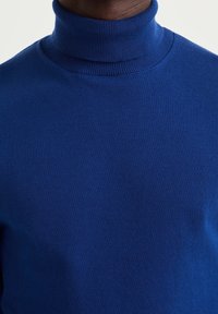 Blå polotröja gjord av stickad tyg, med ribbad halsringning och mjuk textur, utformad för en tät passform runt halsen.