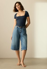 Body a collo quadrato color navy abbinato a culottes di jeans azzurri, con vita media, vestibilità ampia e una semplice cintura nera. Sandali con tacco beige.