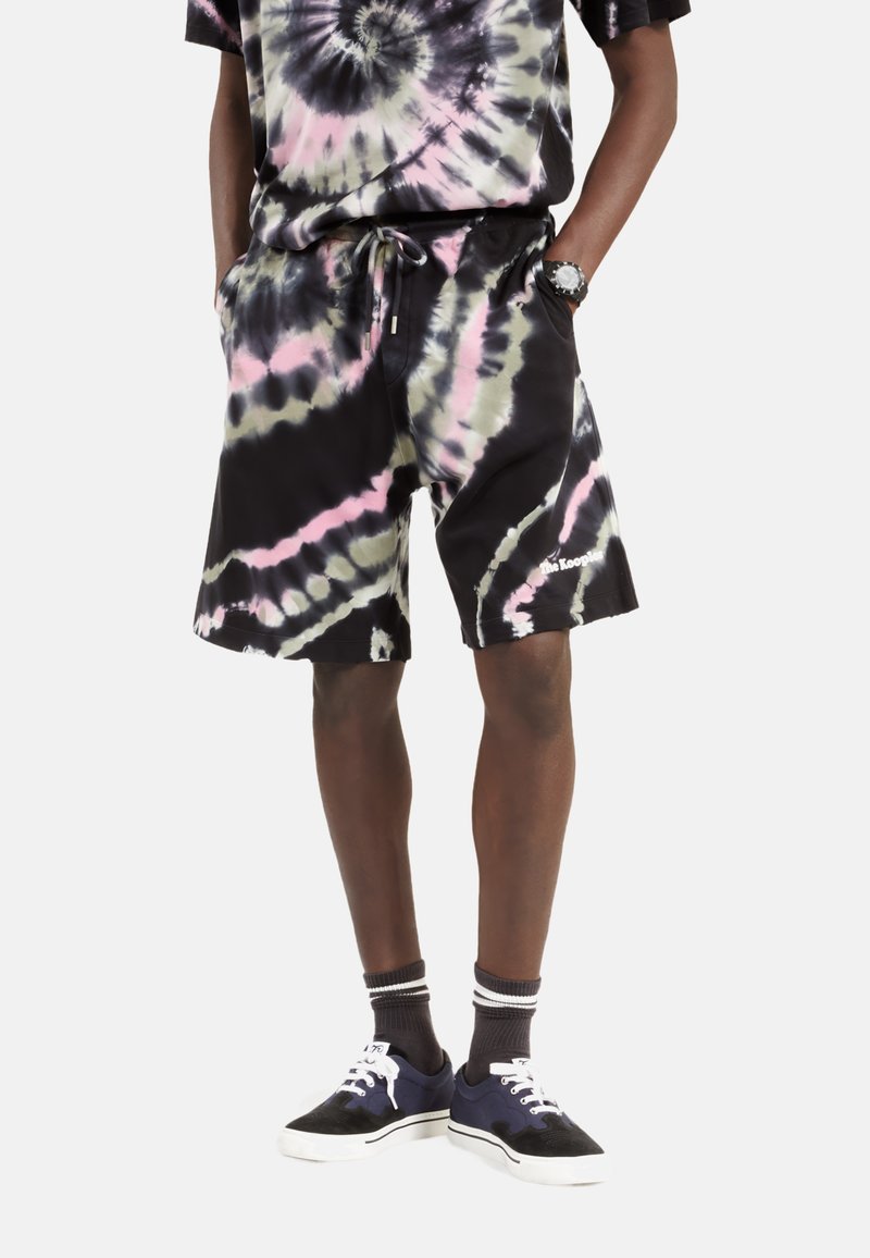 Sorte tie-dye shorts med pink og grønne swirl, kompletteret med en matchende skjorte. Båret med marineblå sneakers og stribede sokker.