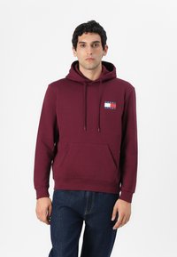 Bordeaux huoodie med snore, frontlomme til h�ænderne og et logo-patch i stof med blå og hvide vandrette striber. Materiale i bomuld.