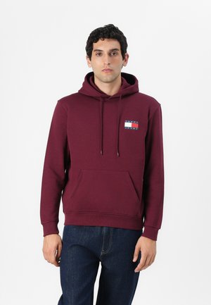 Bordeaux hoodie met trekkoorden, een voorpand kangaroo zak en een stoffen logopatch met blauwe en witte horizontale strepen. Katoenen materiaal.