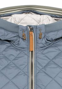 Gequiltte blauwe jas met hoge kraag, voorzien van een voorrits, bruine accenten en contrasterende witte en bruine voering aan de binnenkant.