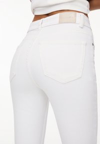 Jeans de denim blanco con un diseño ajustado, bolsillos traseros y una etiqueta en la cintura. Textura suave con detalles de costura sutiles.