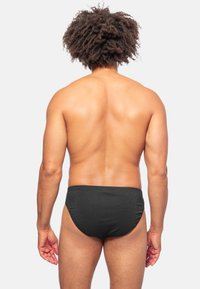 Zwarte zwembroek met een textuurpatroon, elastische tailleband en klassieke snit, gezien vanaf de achterkant tegen een effen achtergrond.