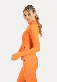 Figursydd orange träningsjacka med hög krage och dragkedja, långa ärmar med tumhål, slät textur, kombinerad med matchande leggings.