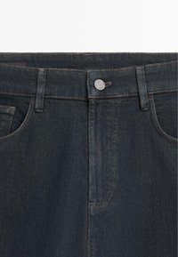 Donkerblauwe spijkerbroek taille met knoopsluiting, riemlussen en zichtbare voorzakken.