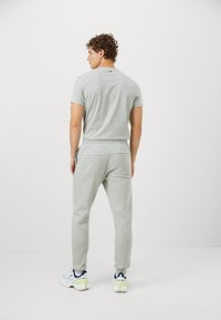 Harmaa kaksiosainen aktiivivaatetus, joka sisältää istuvan lyhythihaisen paidan ja vastaavat verkkarit. Materiaali on pehmeää puuvillasekoitetta ja siinä on joustava vyötärö.