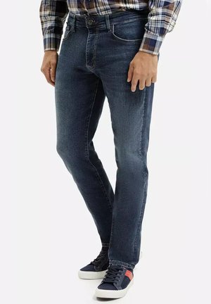 Ciemnoniebieskie dżinsy o slim fit, pięciokomorowym designie, widocznym przeszyciu, zestawione z granatowymi trampkami z czerwonymi akcentami.