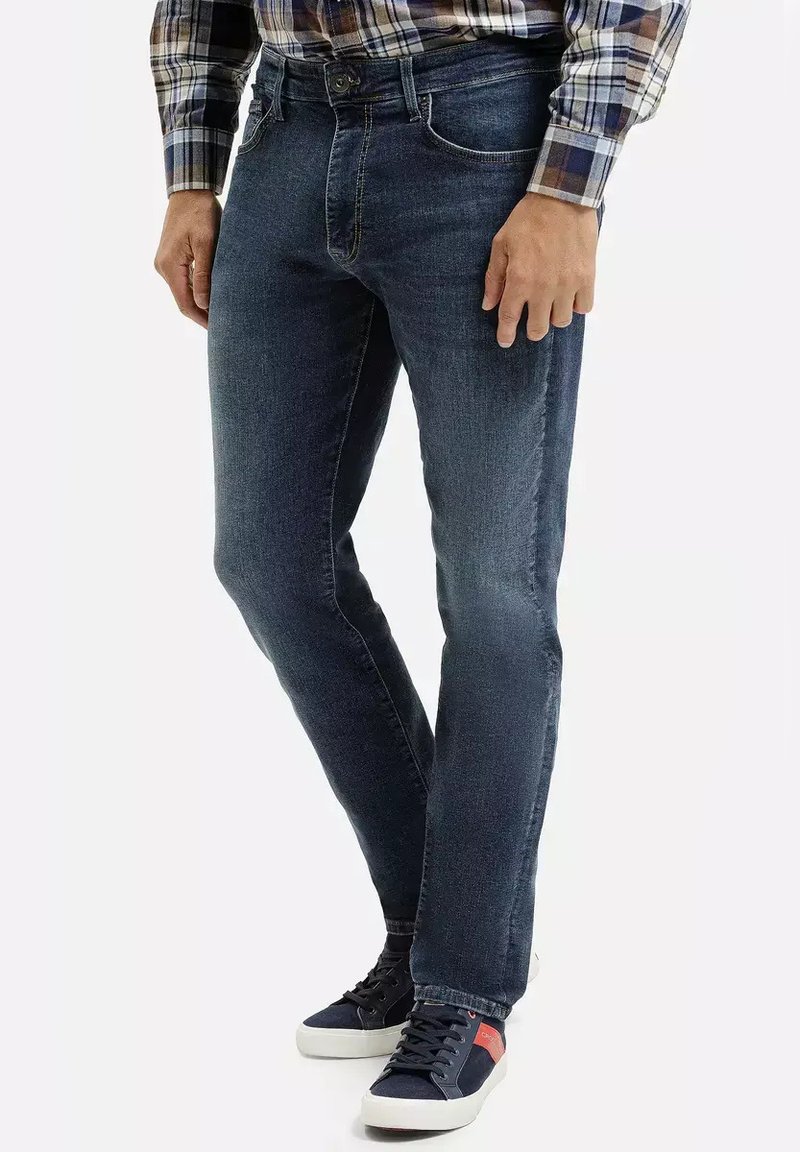 Ciemnoniebieskie dżinsy o slim fit, pięciokomorowym designie, widocznym przeszyciu, zestawione z granatowymi trampkami z czerwonymi akcentami.