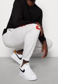 Svart långärmad skjorta, grå sweatpants med röd logotyp och vita Nike Air Force 1 sneakers med svarta och gula accenter. Smart casual stil.